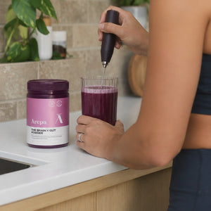 Mixing The Brain x Gut Powder into a glass of water with a frother in the kitchen